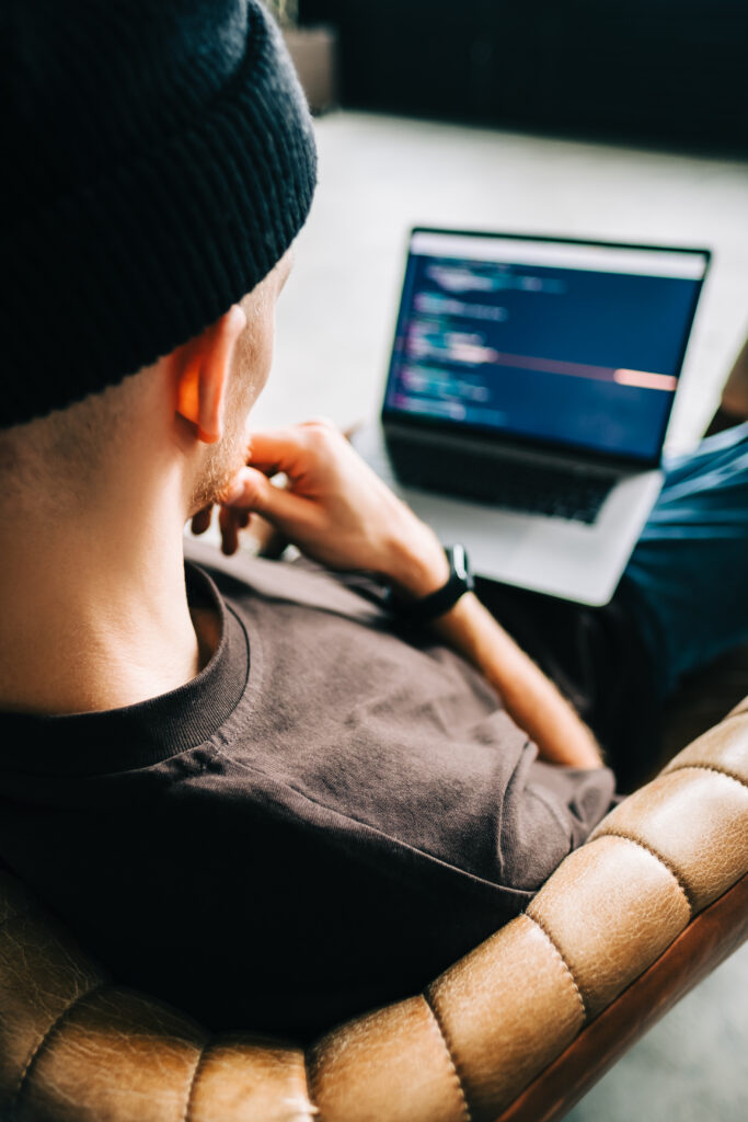 Young man mobile developer writes program code on a computer, programmer work in home office.